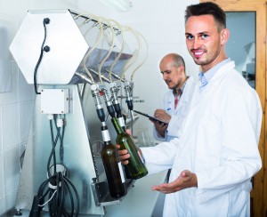 young smiling male winery worker with bottling machinery on factory